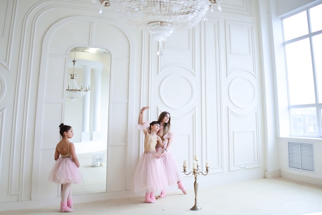 El maestro entrena movimientos de ballet con niñas vestidas de rosa en la habitación