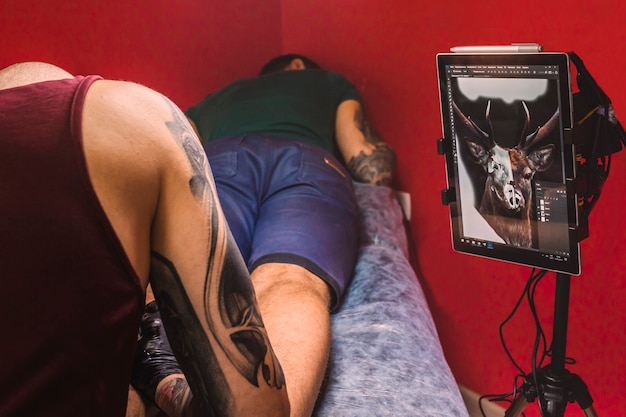 Maestro haciendo tatuaje en estudio con pantalla con borrador