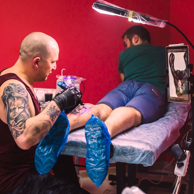 Maestro haciendo tatuaje con la máquina en la pierna