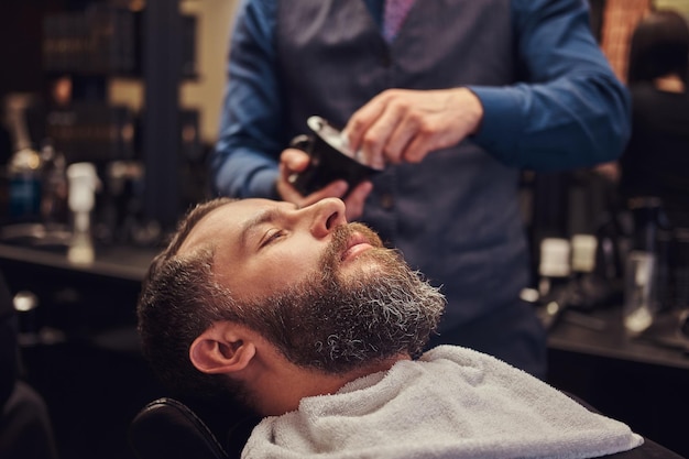Un maestro peluquero prepara la cara para el afeitado, reparte espuma.