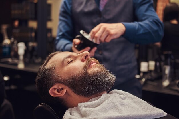 Un maestro peluquero prepara la cara para el afeitado, reparte espuma.