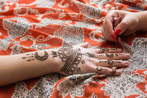 Maestro tatuando pintura mehndi en mano de mujer