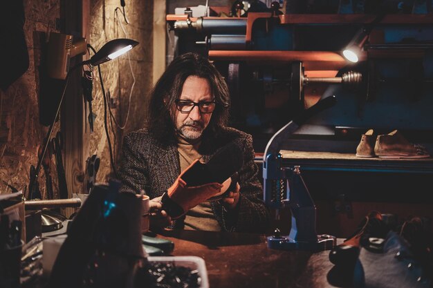 El maestro de zapatos pensativo con anteojos está trabajando en su nueva colección de zapatos en su taller.