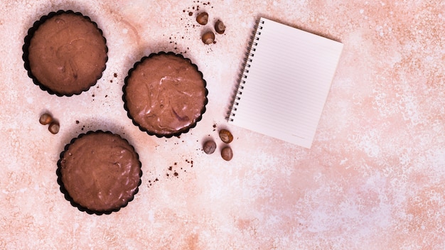 Foto gratuita magdalena de chocolate; bloc de notas de avellana y espiral sobre fondo texturizado