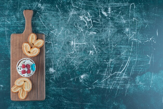 Foto gratuita una magdalena y galletas escamosas agrupadas en un tablero sobre fondo azul. foto de alta calidad