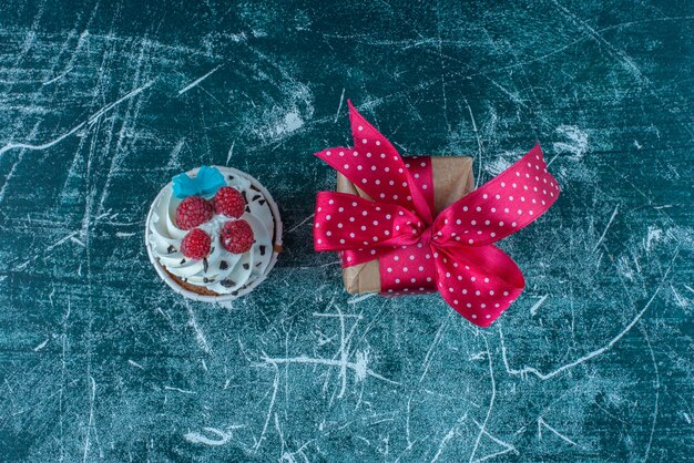 Una magdalena y una pequeña caja de regalo sobre fondo azul. Foto de alta calidad