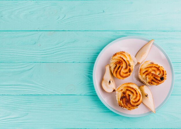 Magdalenas de pera dulce en un plato blanco sobre el fondo de madera turquesa