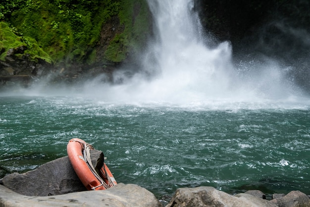 Magnífica cascada y lago rodeado de árboles con un tubo salvavidas que cuelga de una roca