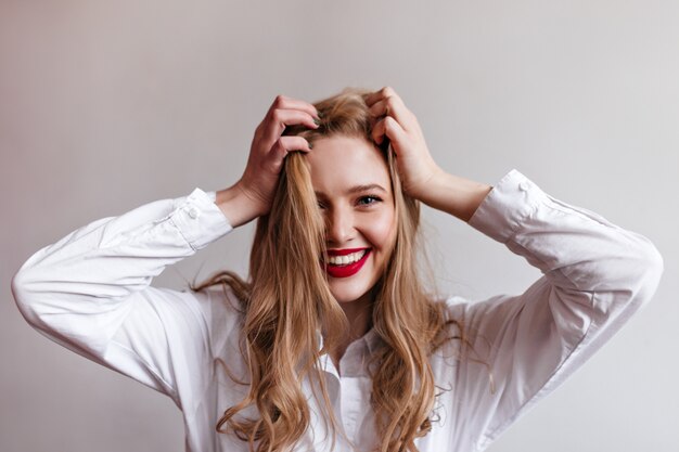 Magnífica joven tocando el cabello rubio con una sonrisa. elegante modelo femenino en camisa.