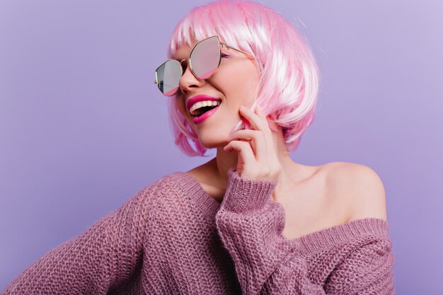 Magnífica jovencita en periwig rosa posando con placer Foto de primer plano interior de una chica muy de moda en peruke aislado en la pared púrpura.