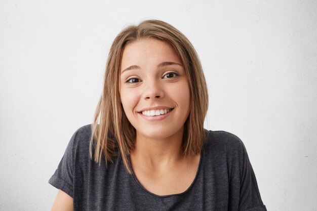 Magnífica mujer bonita con ojos oscuros estrechos y agradable sonrisa encogiéndose de hombros con mirada agradable y dudosa