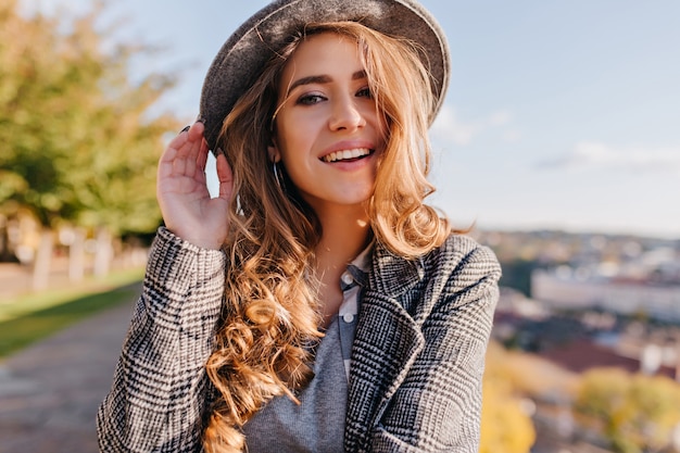 Magnífica mujer joven con hermosos ojos azules posando con sombrero sobre fondo borroso de la ciudad