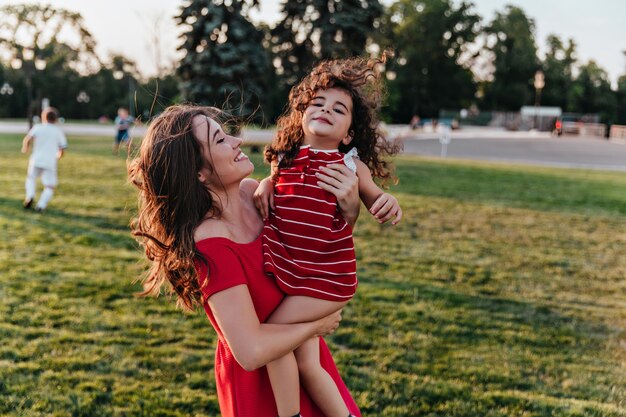 Magnífica mujer joven con su hija y sonriendo. Encantadora dama mirando con amor al niño rizado.