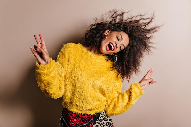 Magnífica mujer negra posando con el signo de la paz Retrato de estudio de una dama africana cantante que viste un suéter amarillo