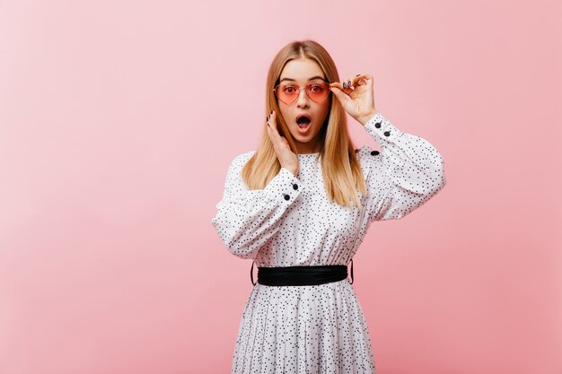 Magnífica mujer sorprendida en vestido largo en rosa. Adorable modelo de mujer con gafas de sol expresando asombro.