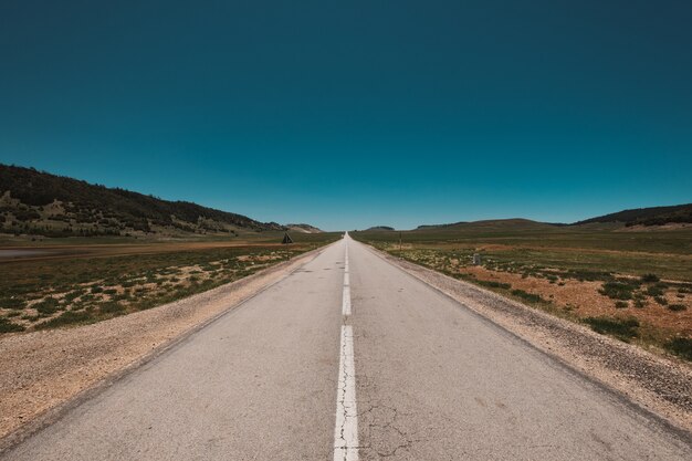 Magnífica vista de una carretera sin fin bajo el cielo azul claro