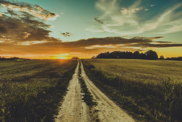 Majestuosa vista de la puesta de sol sobre un paisaje con un camino sin asfaltar que desaparece en el horizonte