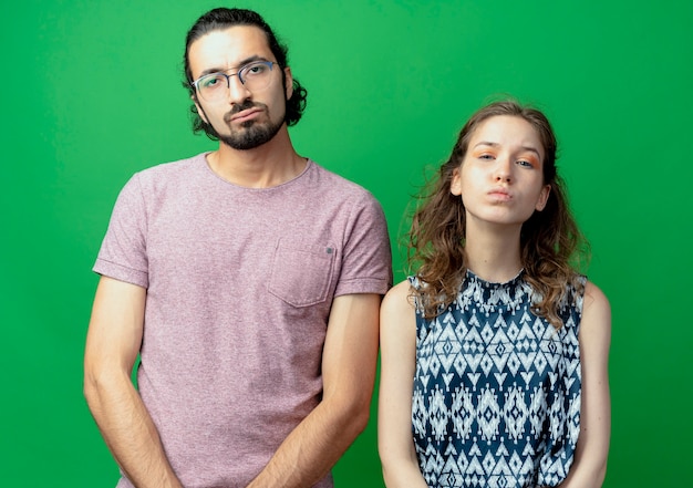 Malestar joven pareja hombre y mujer mirando a la cámara con expresión triste en los rostros de pie sobre fondo verde