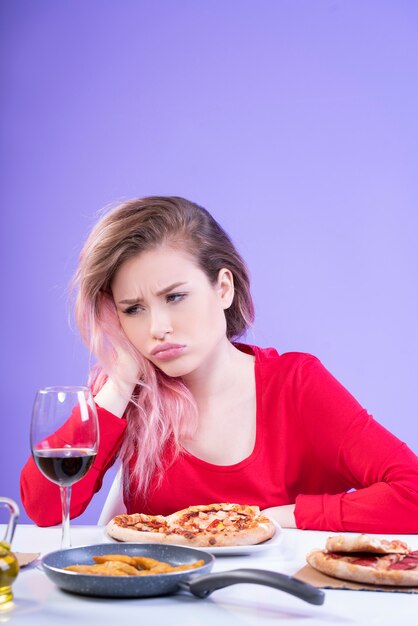 Malestar mujer sentada a la mesa con una copa de vino tinto y pizza