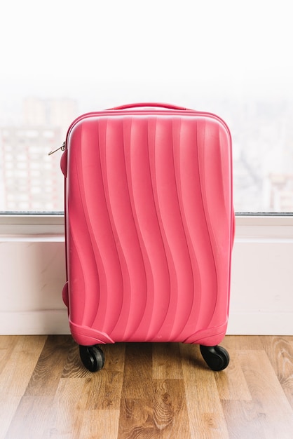 Foto gratuita maleta de viaje rosa de plástico con ruedas sobre suelo de madera.
