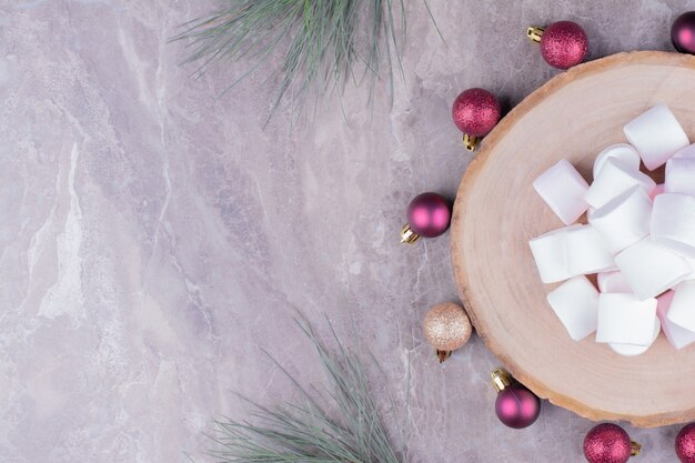 Malvaviscos blancos en una bandeja de madera con bolas rojas de Navidad alrededor