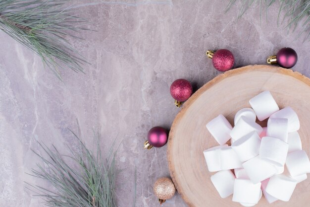 Malvaviscos blancos sobre tabla de madera con bolas de Navidad alrededor.