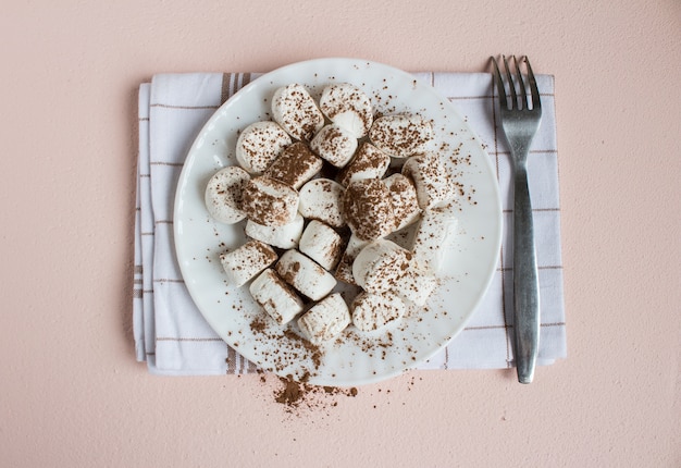 Foto gratuita malvaviscos espolvoreados con cacao en un plato blanco con un tenedor sobre una toalla. comida dulce vista superior