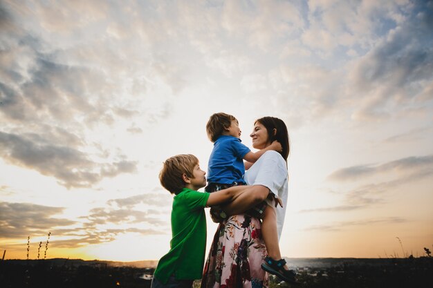 Mamá abraza con sus dos pequeños hijos tiernos de pie en los rayos.