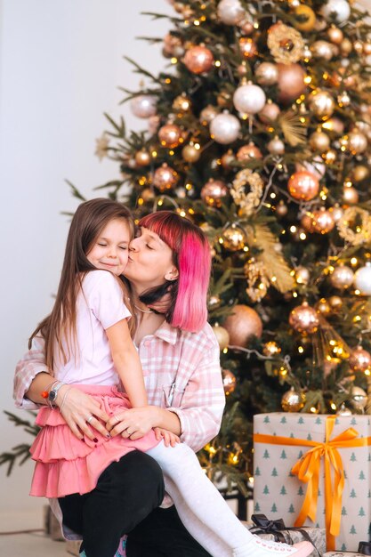 Mamá alegre y linda hija divirtiéndose cerca del árbol de Navidad
