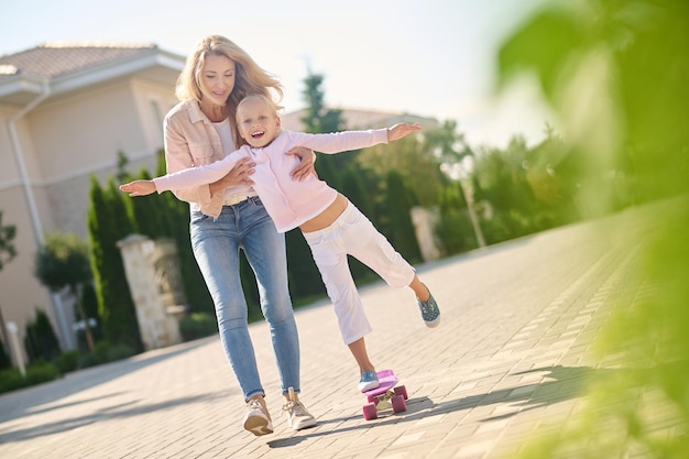 Mamá ayudando a su hija a andar en patineta