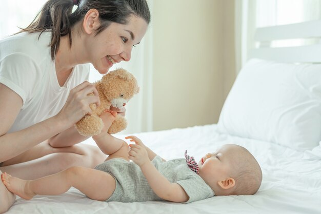 Mamá y bebé felizmente se burlan mutuamente en una cama blanca.