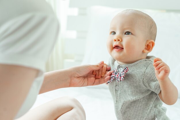 Mamá y bebé felizmente se burlan mutuamente en una cama blanca.