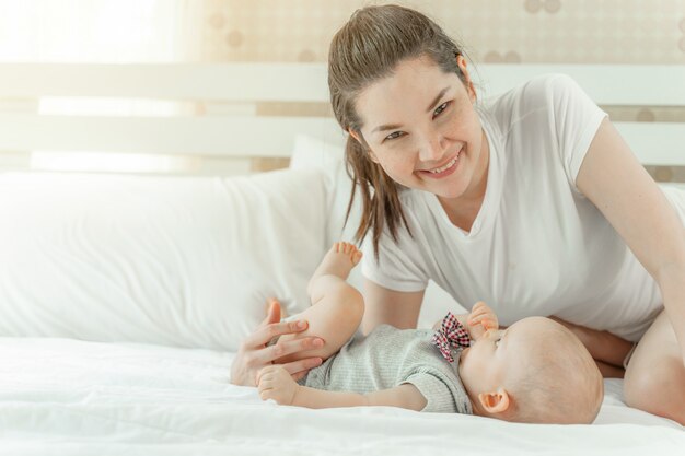 Mamá y bebé felizmente se burlan mutuamente en una cama blanca.