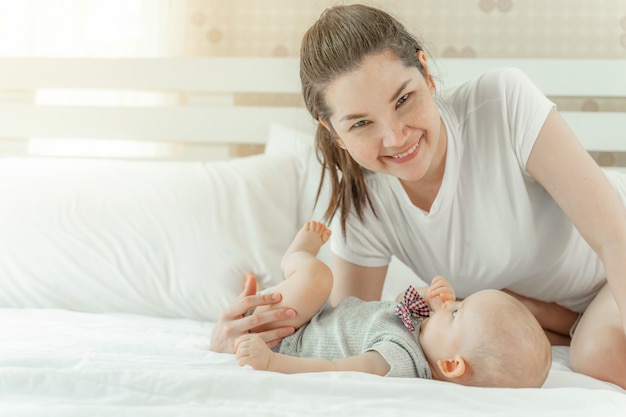 Mamá y bebé felizmente se burlan mutuamente en una cama blanca.