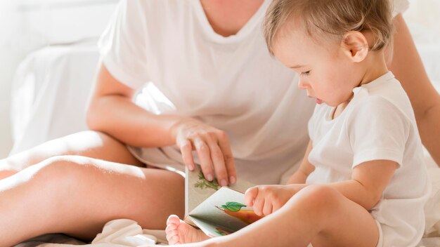 Mamá y bebé sentado en la cama con libro