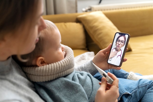 Mamá cuidando a su hijo y teleconsultando con el médico