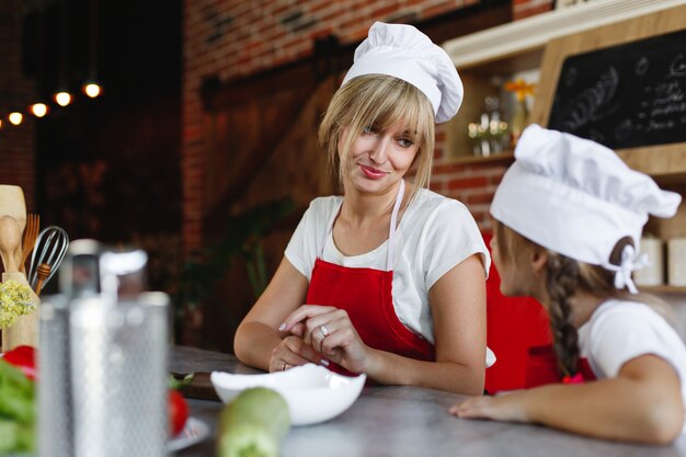 Mamá e hija se divierten en la cocina cocinando diferentes verduras para una cena