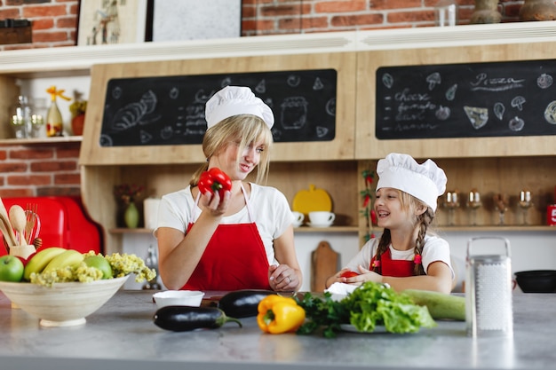 Mamá e hija se divierten en la cocina cocinando diferentes verduras para una cena