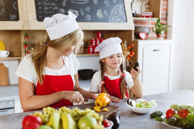 Mamá e hija se divierten en la cocina cocinando diferentes verduras para una cena