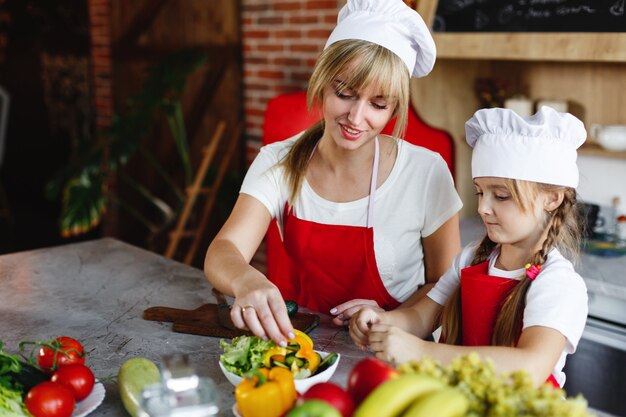 Mamá e hija se divierten en la cocina cocinando diferentes verduras para una cena