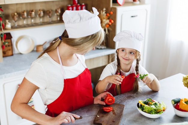 Mamá e hija se divierten en la cocina cocinando diferentes verduras para una cena