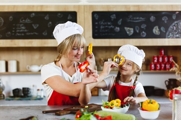 Mamá e hija se divierten en la cocina cocinando diferentes verduras para una cena