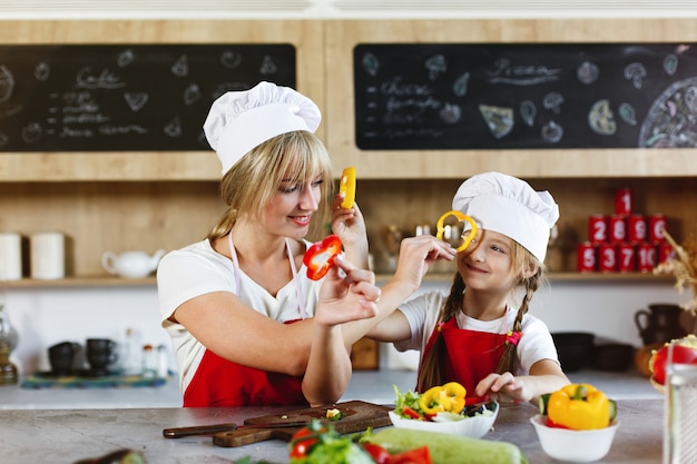 Mamá e hija se divierten en la cocina cocinando diferentes verduras para una cena