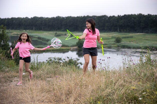 Mamá e hija se divierten juntas, hacen grandes pompas de jabón, actividades recreativas familiares al aire libre.