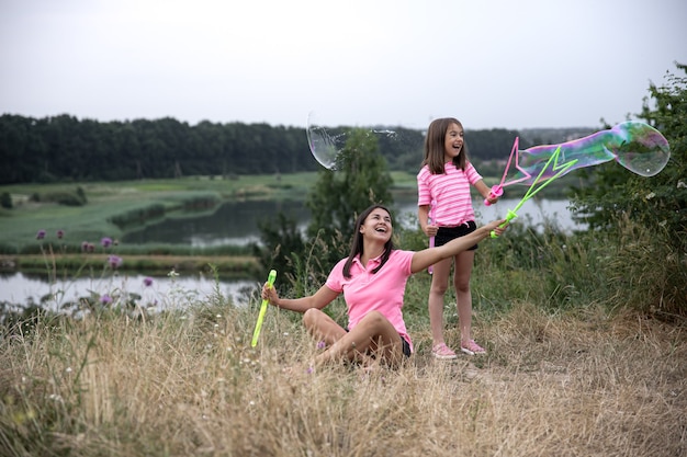 Mamá e hija se divierten juntas, hacen grandes pompas de jabón, recreación al aire libre.