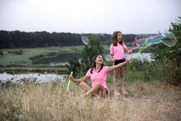 Mamá e hija se divierten juntas, hacen grandes pompas de jabón, recreación al aire libre.