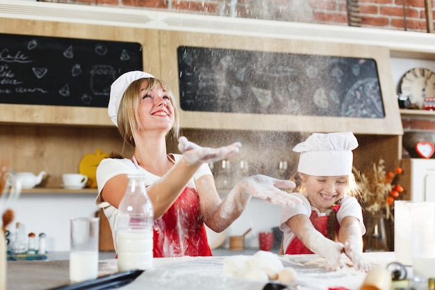 Mamá e hija con la misma ropa se divierten preparando una masa en una cocina acogedora