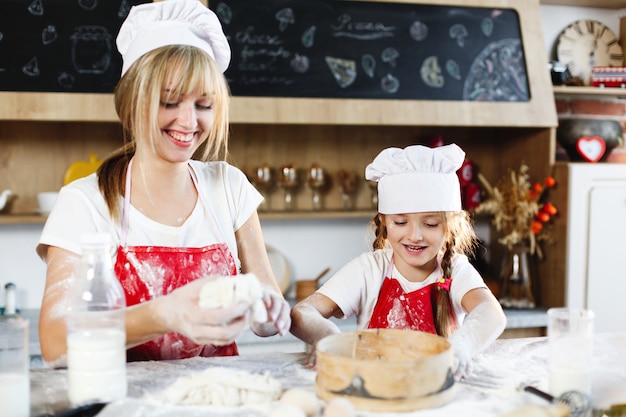 Mamá e hija con la misma ropa se divierten preparando una masa en una cocina acogedora