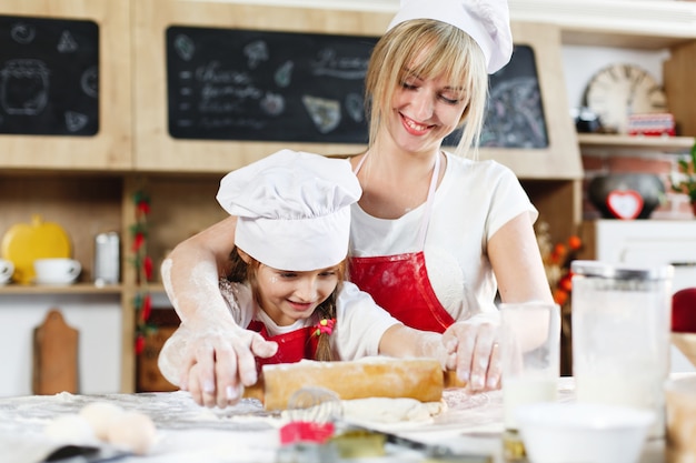 Foto gratuita mamá e hija con la misma ropa se divierten preparando una masa en una cocina acogedora