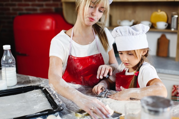 Mamá e hija con la misma ropa se divierten preparando una masa en una cocina acogedora